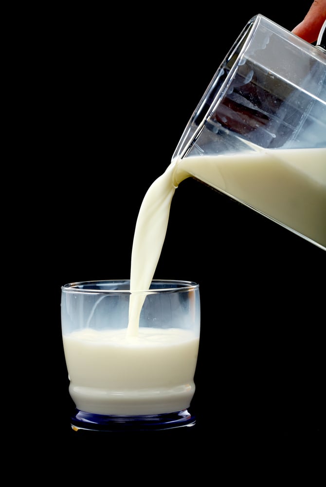 glass of milk being poured over a black background